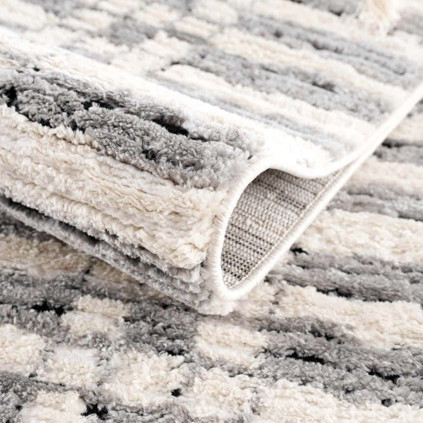 Close-up of the Nava Area Rug, showcasing its beige, black, and bone geometric pattern and soft, textured pile. Fold