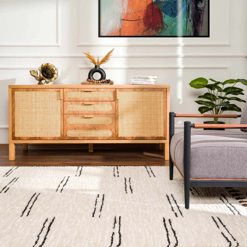 Living room scene with a Riad Black Striped White Rug, wood cabinet, gray chair, and colorful art. Roomscene-Rectangle
