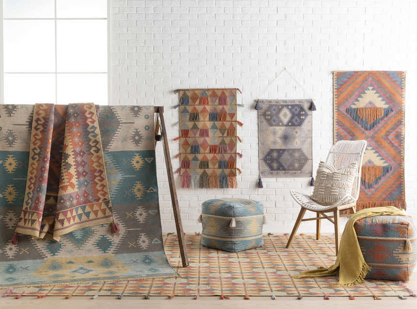Eclectic room scene with Heth Carpet, woven wall hangings, poufs, and a white chair against a white brick wall. Styleshot