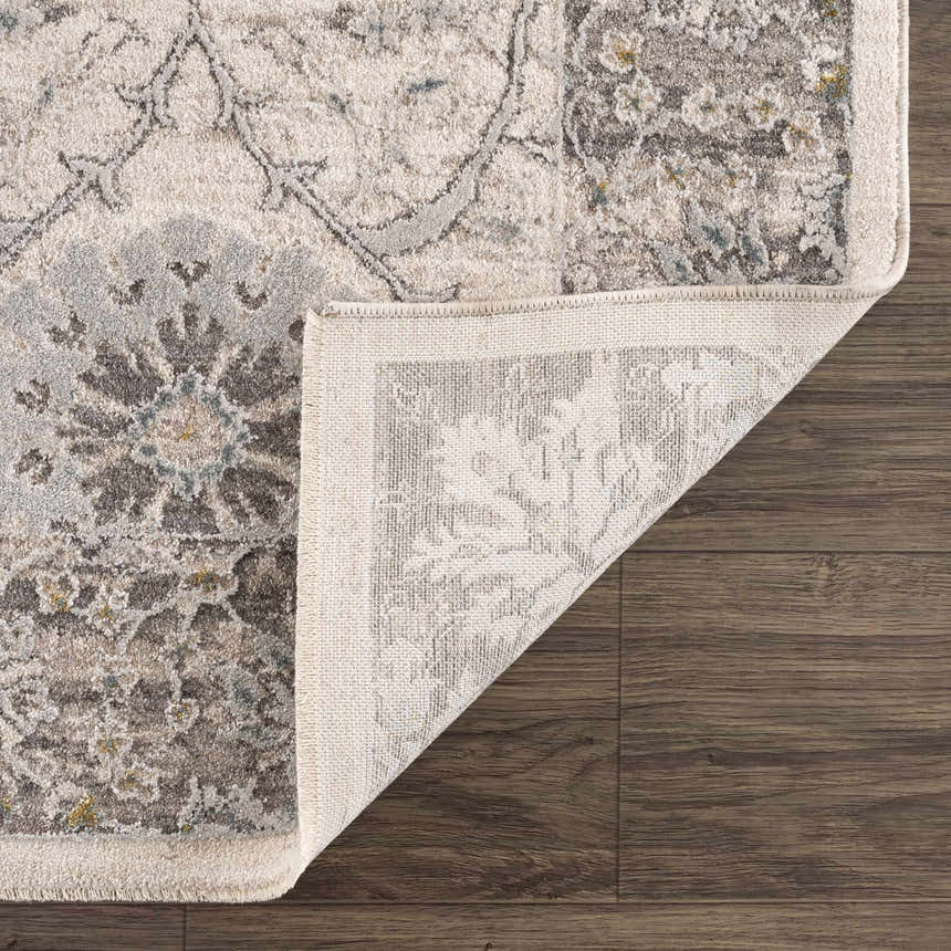 Close-up of Gauge Cream & Gray Blue Rug showing floral pattern, fringe detail, and backing on dark wood floor. Fold