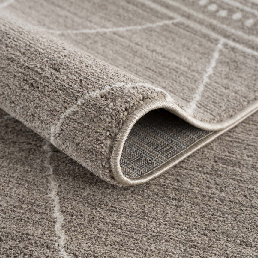 Close-up of the Kami Area Rug showing its dark beige color, ivory geometric pattern, and soft, textured pile. Fold