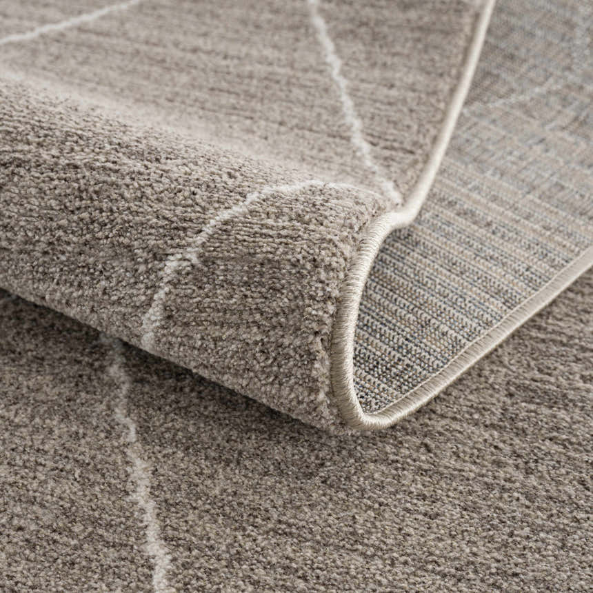 Close-up of the Kami Area Rug, a dark beige rug with ivory geometric lines and a soft, textured pile. Fold