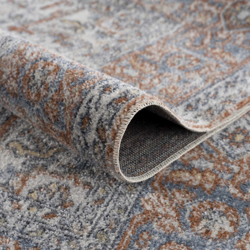 Close-up of the Aila Traditional Design Washable Rug featuring blue, mustard, off-white, and tan vintage patterns. Fold