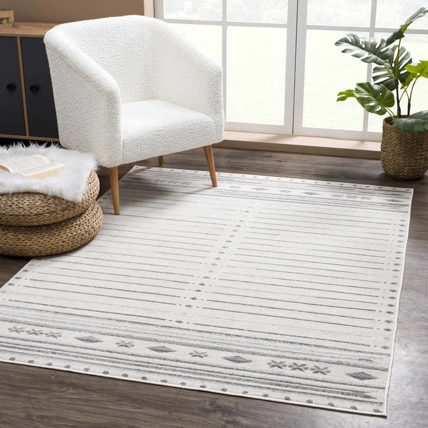 Living room scene with Tigri Aztec Ivory & Gray rug, white sherpa chair, woven ottoman, and monstera plant near a bright window. Roomscene-Rectangle