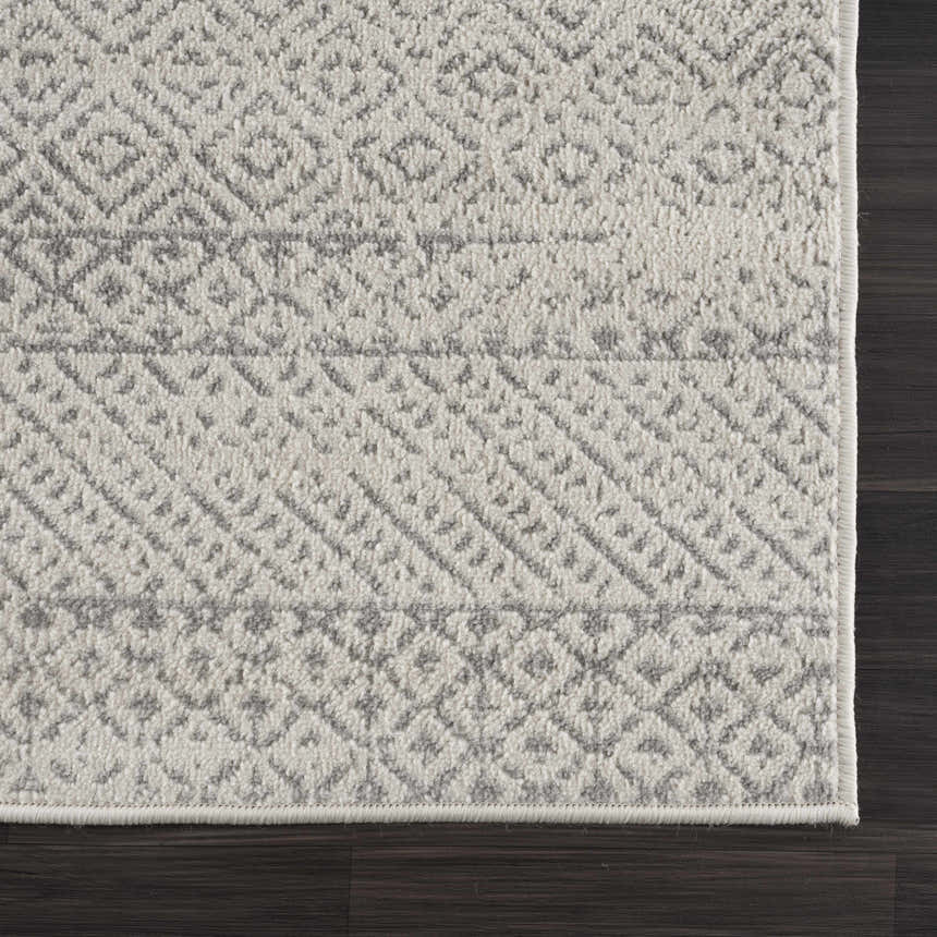 Close-up of Tigri Aztec Ivory & Gray area rug showing its geometric pattern and soft, textured weave on dark wood floor. Corner
