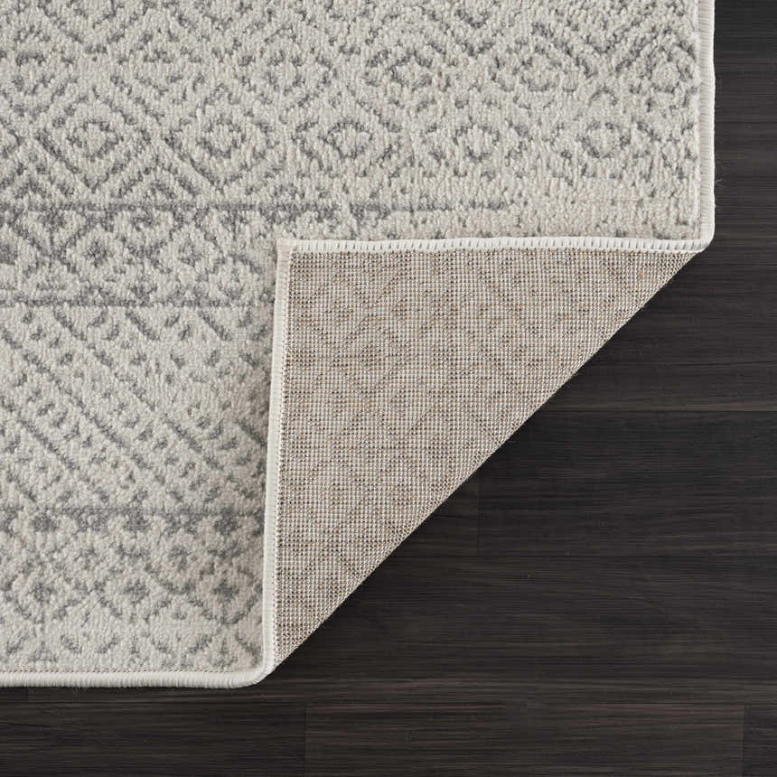 Close-up of Tigri Aztec Ivory & Gray Area Rug showing geometric pattern, soft texture, and rug backing on dark wood floor. Fold