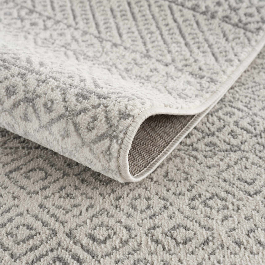 Close-up of Tigri Aztec Ivory & Gray Area Rug showing geometric pattern, soft texture, bound edge, and backing. Fold