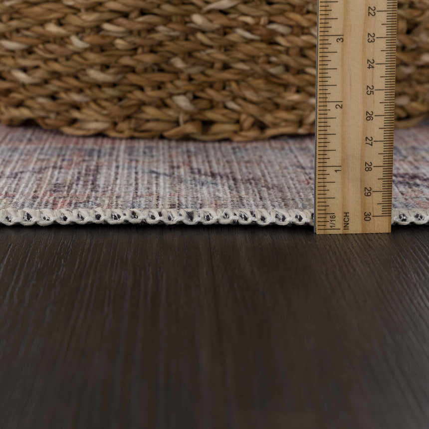 Close-up of the Morcott Peach Washable Area Rug showing the rug thickness with a ruler, and woven texture. Pile