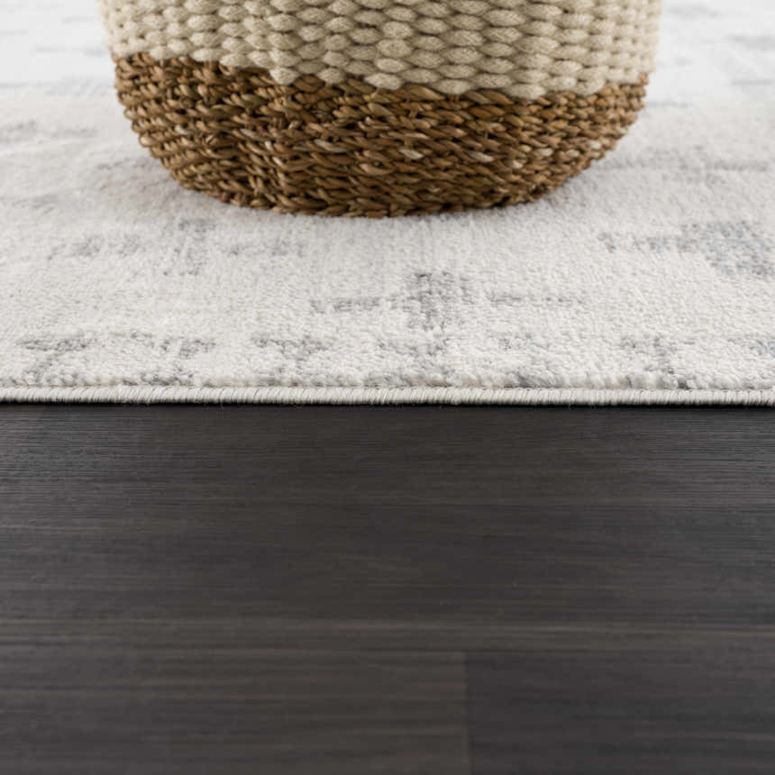 Close-up of the Tigris Swiss Cross Ivory & Gray Area Rug with a basket on top, showing texture and geometric pattern. Styleshot