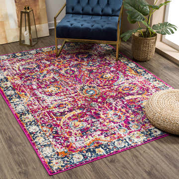 Living room scene with a vibrant Vick Area Rug in burgundy, orange, navy, and mustard under a blue chair and next to a woven pouf. Roomscene-Rectangle