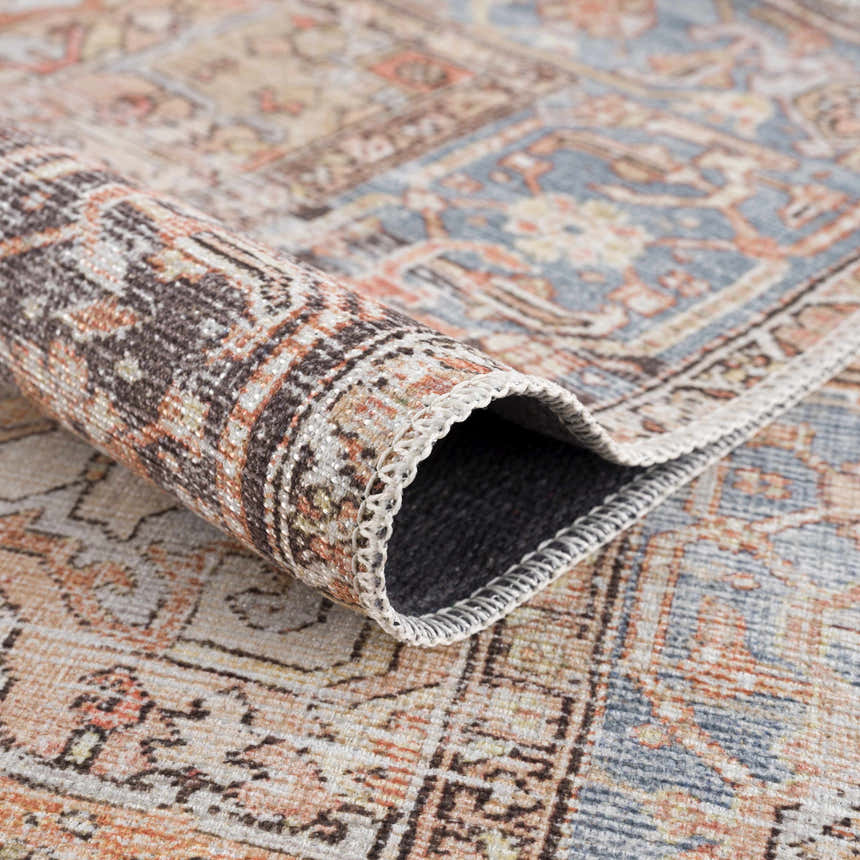 Close-up of the Eira Distressed Washable Rug showing its charcoal, blue, orange, and off-white Persian-style pattern and texture. Fold