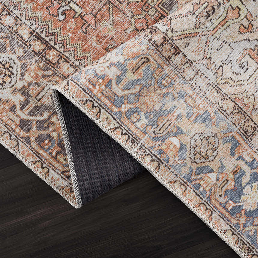 Close-up of the Eira Distressed Washable Rug. Features a vintage Persian pattern in charcoal, light blue, orange, and off-white. Fold