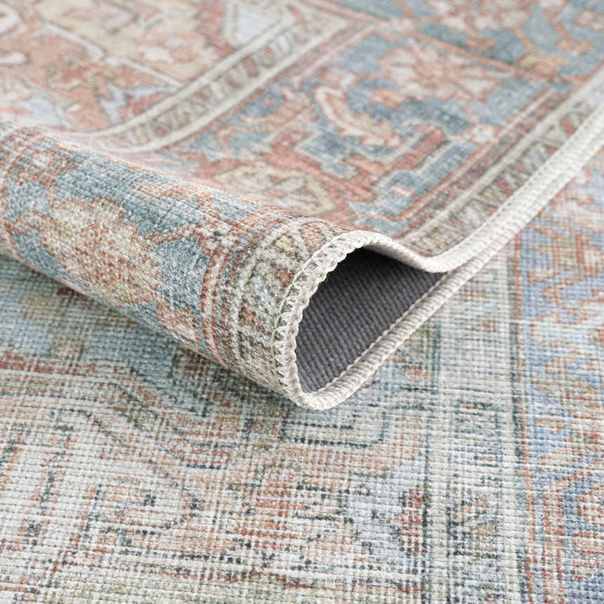 Close-up of the Rust Maayon Washable Rug showing its brick red, blue, and brown traditional design and machine-woven texture. Fold