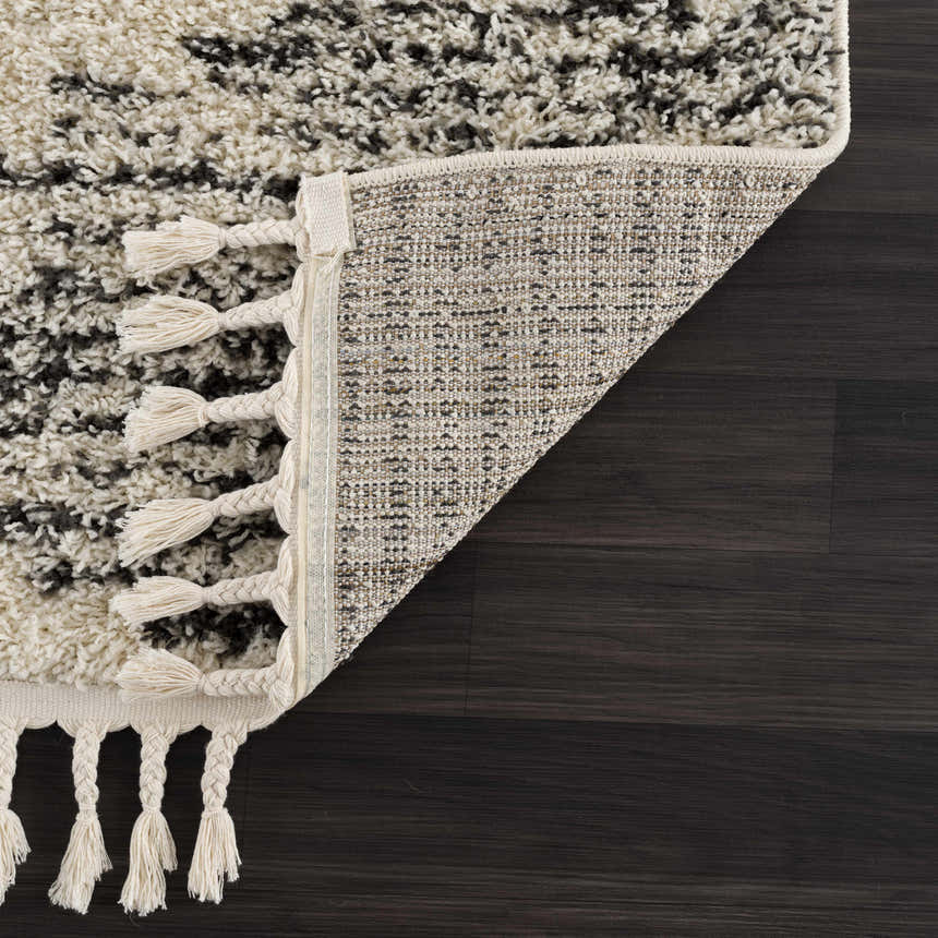 Close up of the Howth Area Rug showing bone and dark gray shag texture and braided tassels. Corner