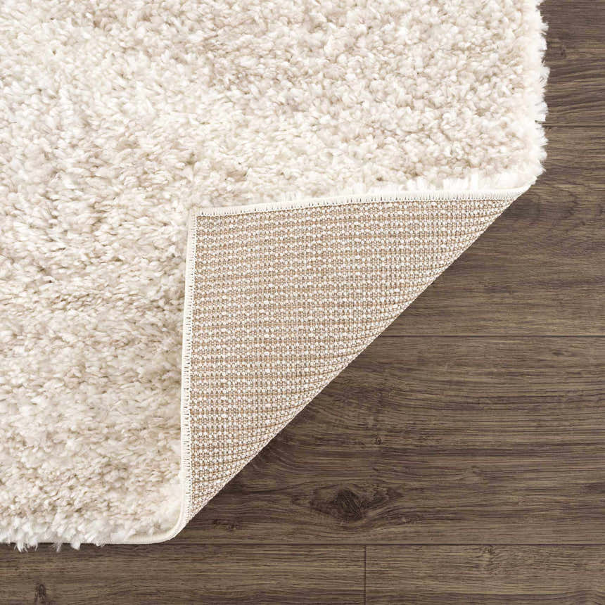Close-up of the Hauteloom Trunding Plush Rug in Light Beige showing its shag texture and durable backing on a wood floor. Fold