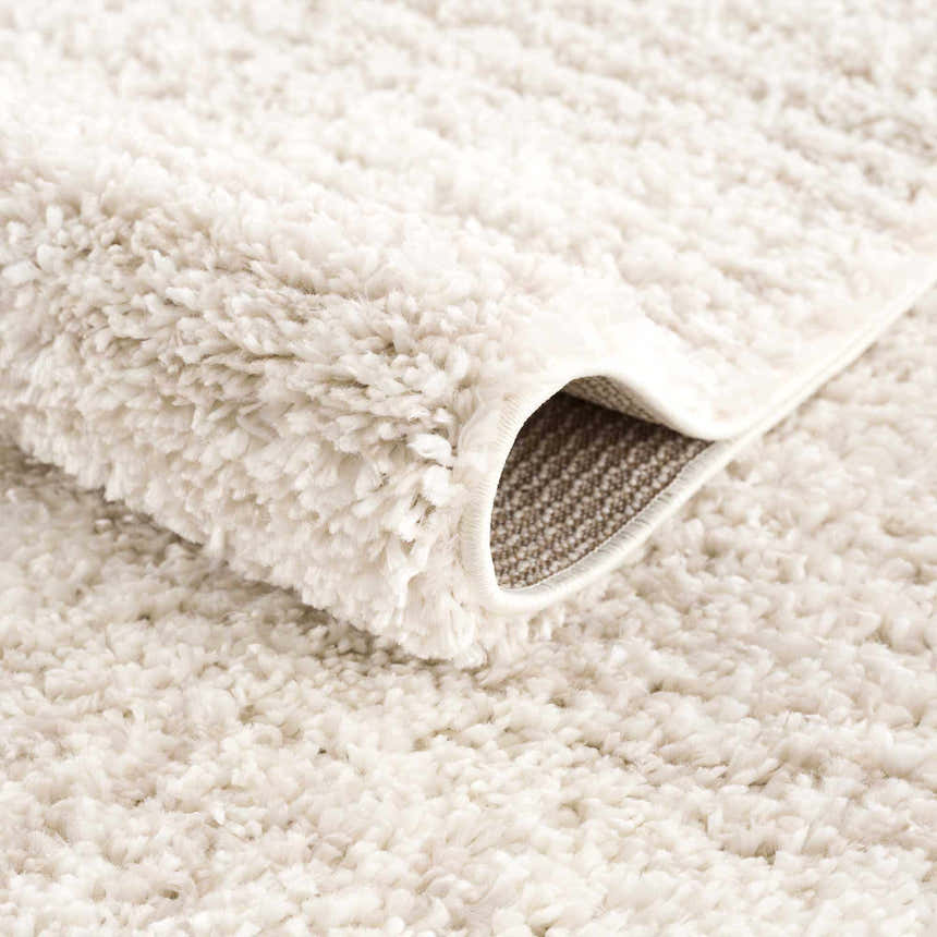 Close-up of the Hauteloom Trunding Plush Rug in Light Beige. Shows the shag texture and woven backing detail. Fold