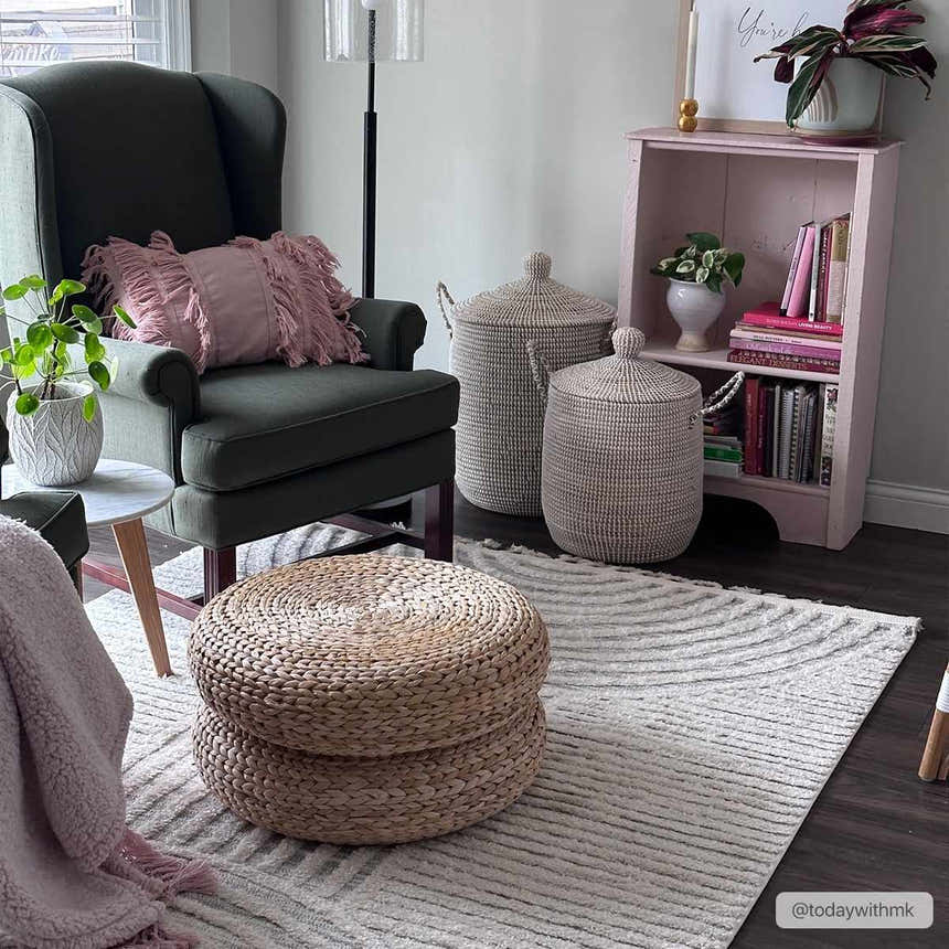 Living room scene with a Dauin 3D Rainbow Area Rug, dark green armchair, woven baskets, and pink bookshelf. Roomscene-Rectangle