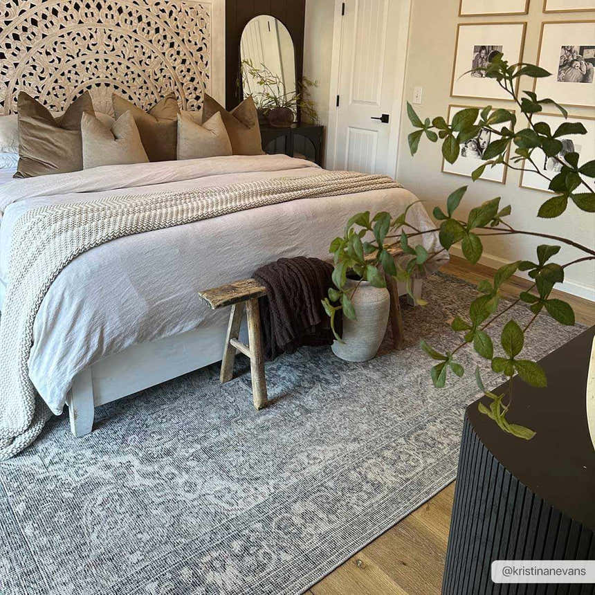 Bedroom scene with a Greenpoint Dusty Blue Washable Rug, wooden floors, neutral bedding, and a decorative wooden headboard. Roomscene-Rectangle