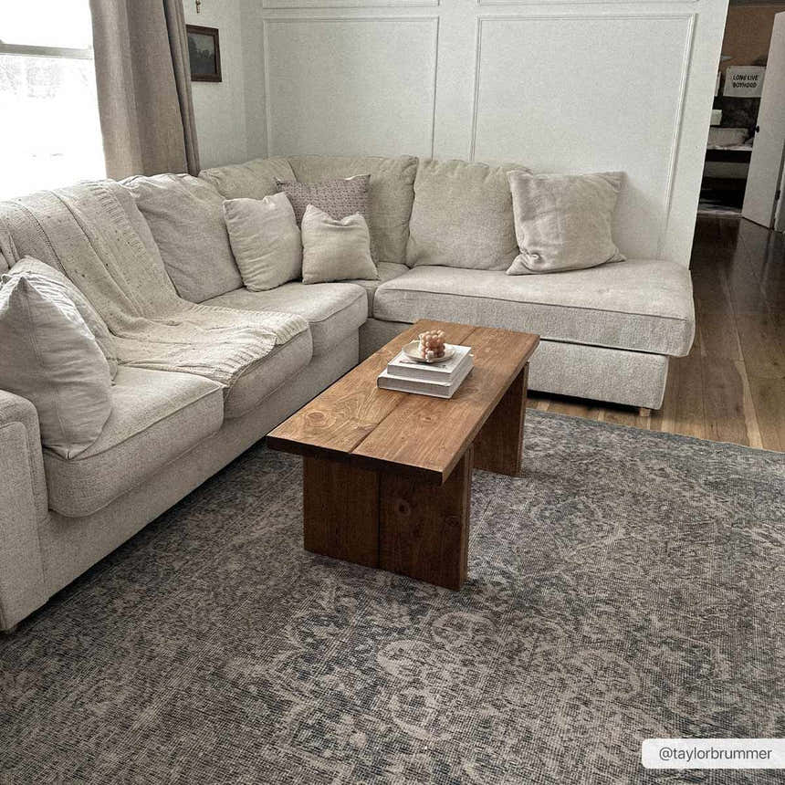 Living room scene with a Greenpoint Dusty Blue Washable Rug under a rustic wood coffee table and beige sectional sofa. Roomscene-Rectangle