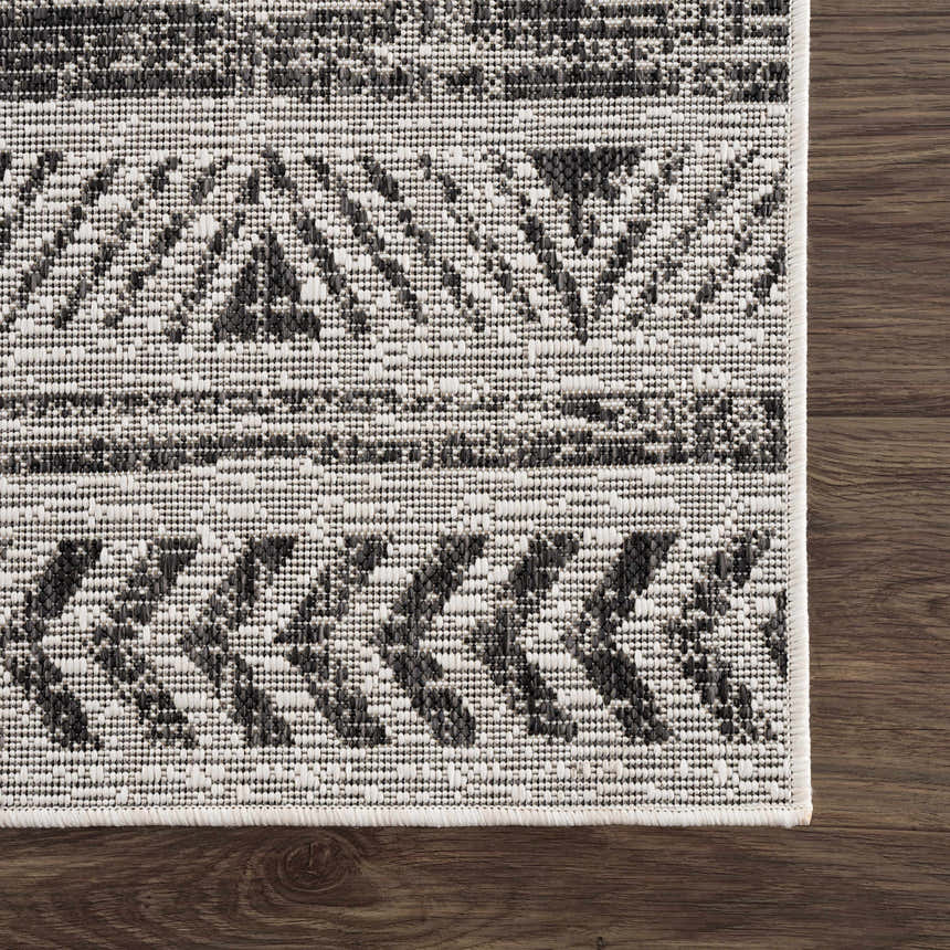Close-up of the Catrine Indoor & Outdoor Rug. Bohemian style rug in black, charcoal, and off-white colors on dark wood floor. Swatch