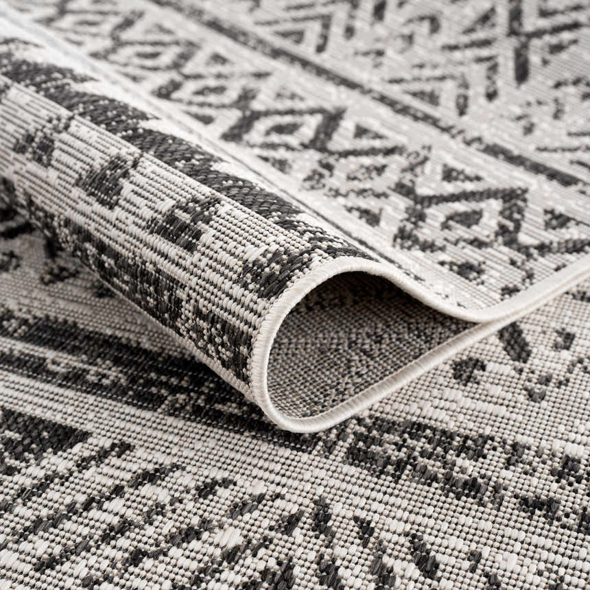 Close-up of the Catrine Indoor & Outdoor Rug. Black, charcoal, and off-white bohemian pattern. Machine woven texture. Fold