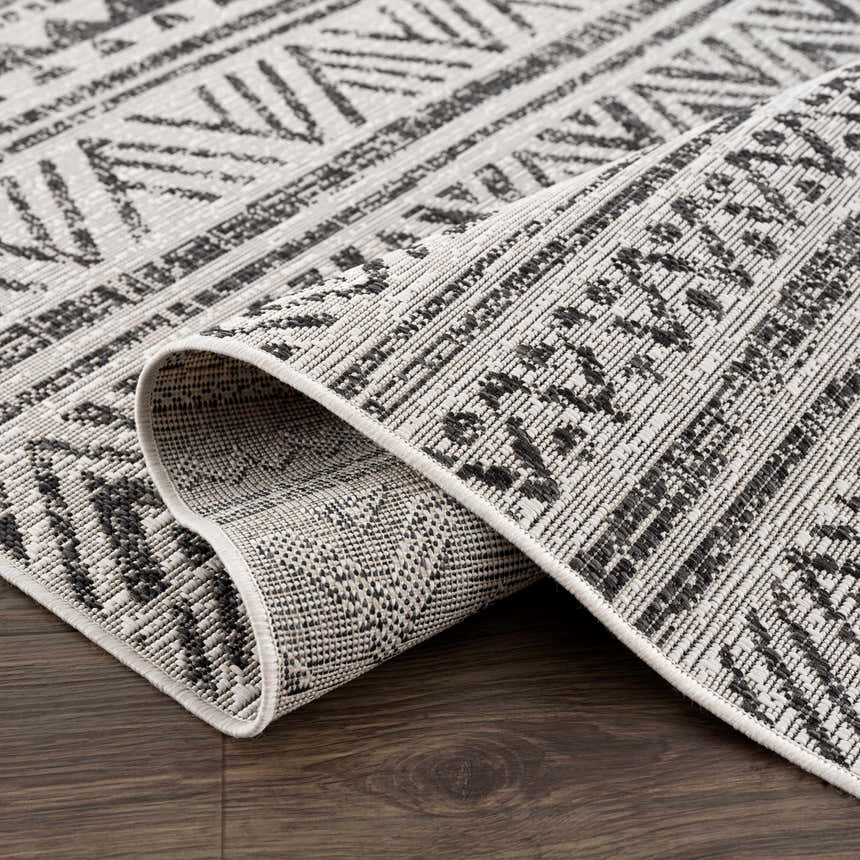 Close up of the black and white geometric patterned Catrine Indoor & Outdoor Rug on a wood floor. Fold