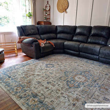 Living room scene with a blue and rust Ezri Cream Washable Area Rug under a large, dark sectional sofa. Roomscene-Rectangle