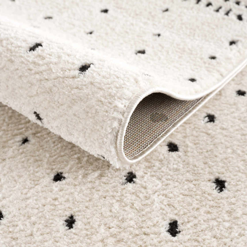 Close up of the Julie Area Rug showing its beige, fluffy texture and black polka dot geometric pattern. Fold