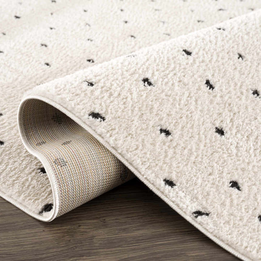 Close-up of the Julie Area Rug in beige with black polka dots, showing the rug's texture and backing. Fold