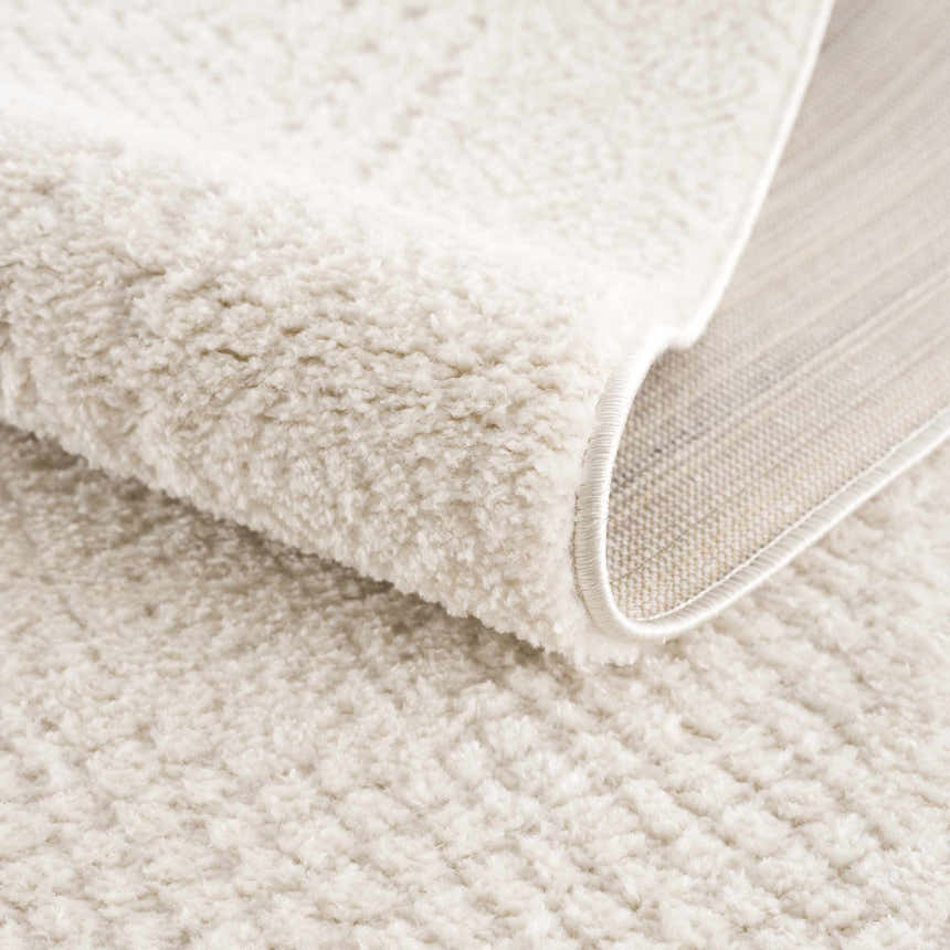 Close-up of the plush, ivory Julio Area Rug showing its soft texture and machine-woven construction. Fold