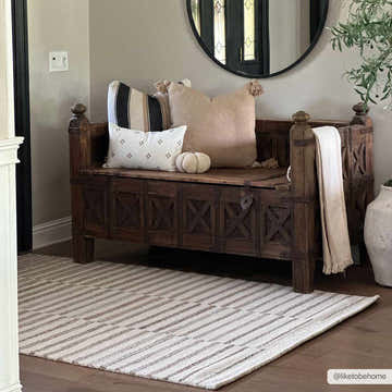 Entryway with a Gawel Brown area rug, wooden bench, pillows, and round mirror, creating a cozy, neutral-toned space. Roomscene-Rectangle