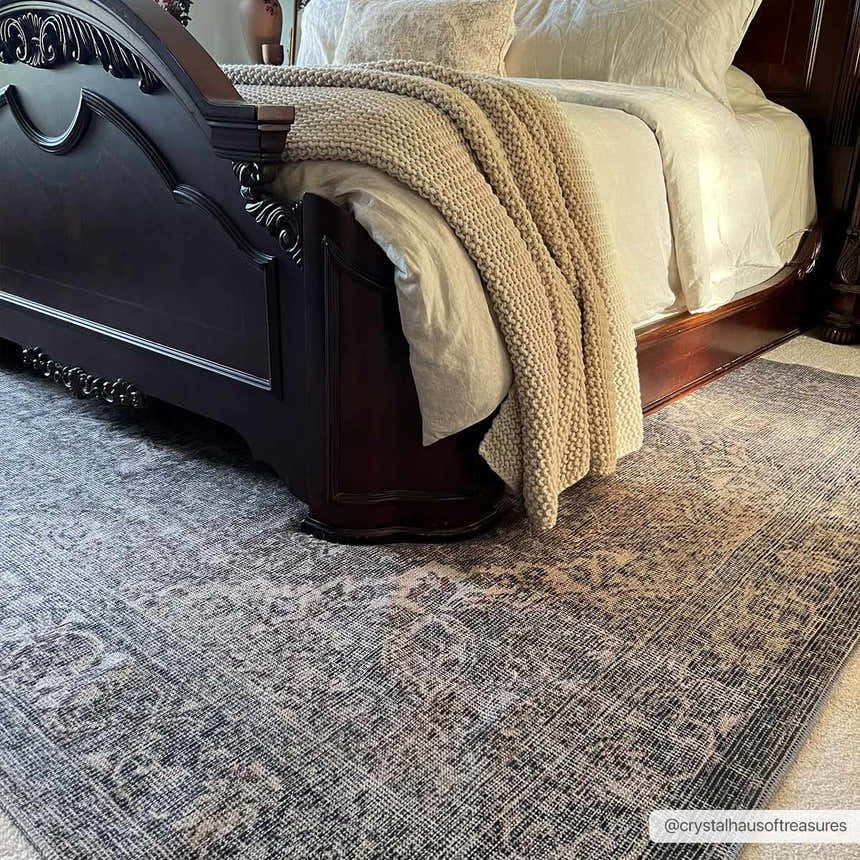 Bedroom scene with a Greenpoint Dusty Blue Washable Rug under a dark wood bed with beige bedding and a knit throw. Roomscene-Rectangle