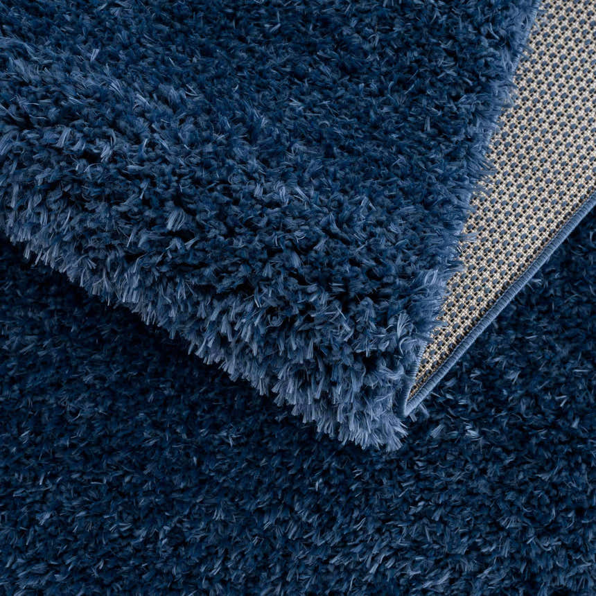 Close-up of the plush texture and backing of the Faina Solid Dark Blue Shag Washable Area Rug. Fold