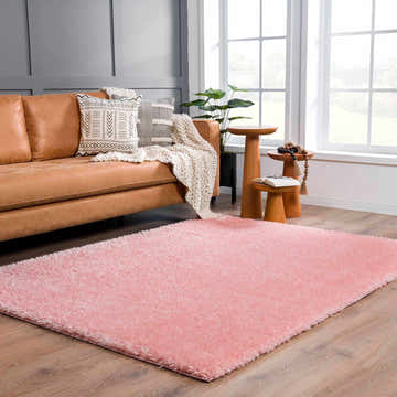 Living room scene with a Faina Solid Pink Shag rug, tan leather sofa, wood side tables, and a large window. Roomscene-Rectangle