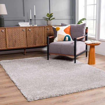 Living room scene with a light gray Faina Solid Shag Rug, gray chair, wood cabinet, and light wood floors. Roomscene-Rectangle