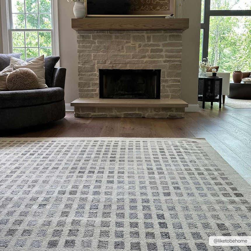 Living room scene with a beige Harib Area Rug, stone fireplace, wood floors, and gray swivel chair. Roomscene-Rectangle