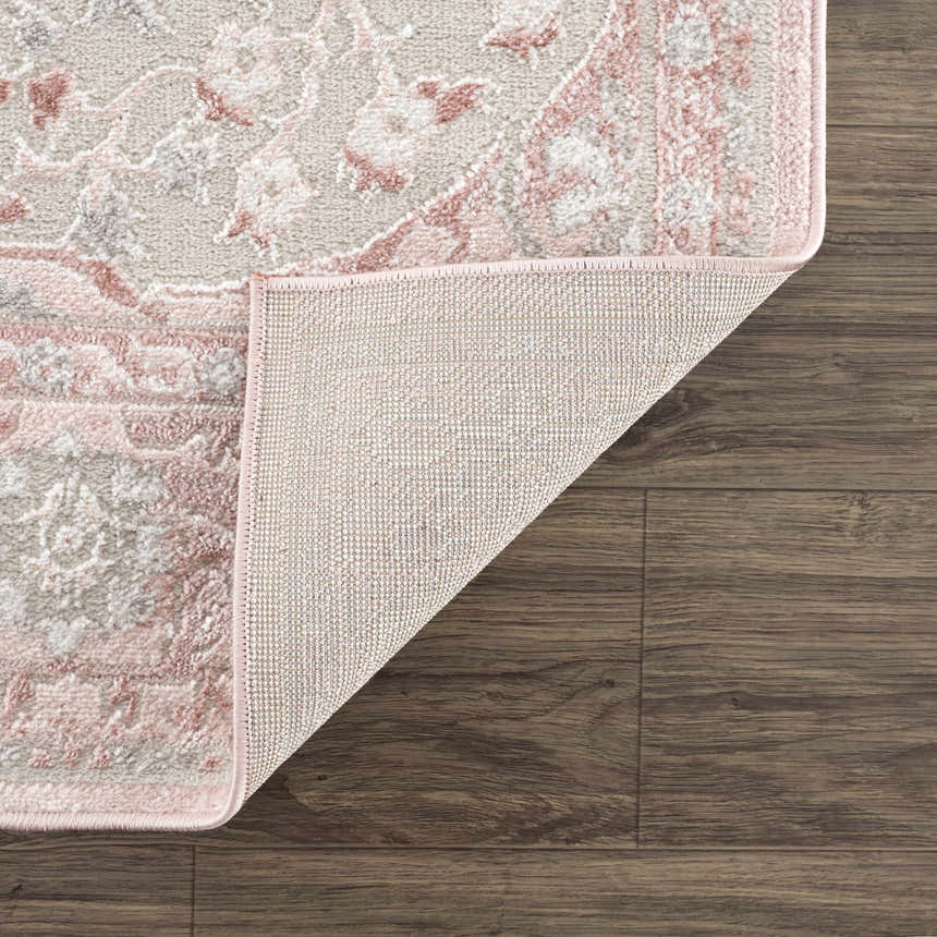 Close-up of the Zora Pink Area Rug showing its gray and pink traditional pattern and woven backing on wood floors. Fold