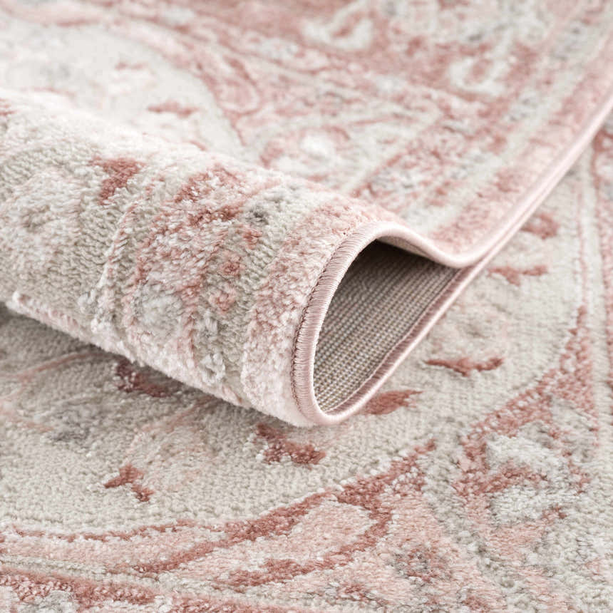 Close-up of the Zora Pink Area Rug showing its traditional vintage pattern, soft texture, and gray and pink colors. Fold