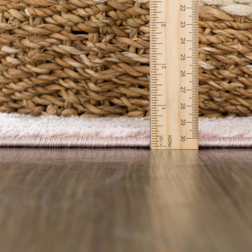 Close-up of the Zora Pink Area Rug showing its pile height with a ruler and a woven basket in the background. Pile