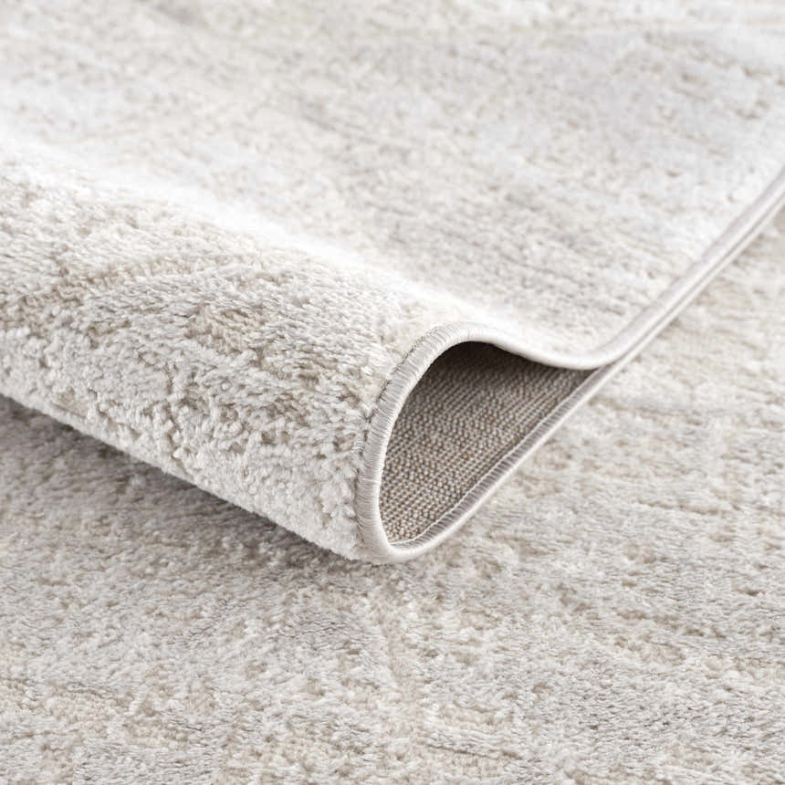 Close-up of the textured, gray Basia Area Rug. Shows the rug's backing and binding detail. Modern abstract design. Fold