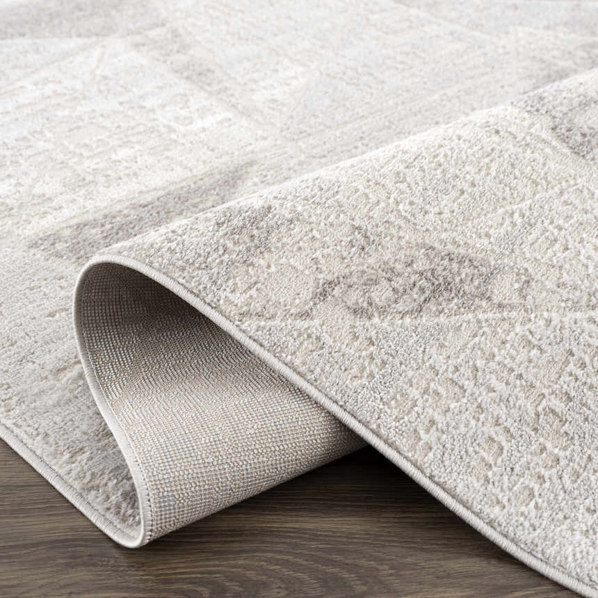 Close-up of the textured, light gray Basia Area Rug showing its geometric pattern and woven backing. Fold