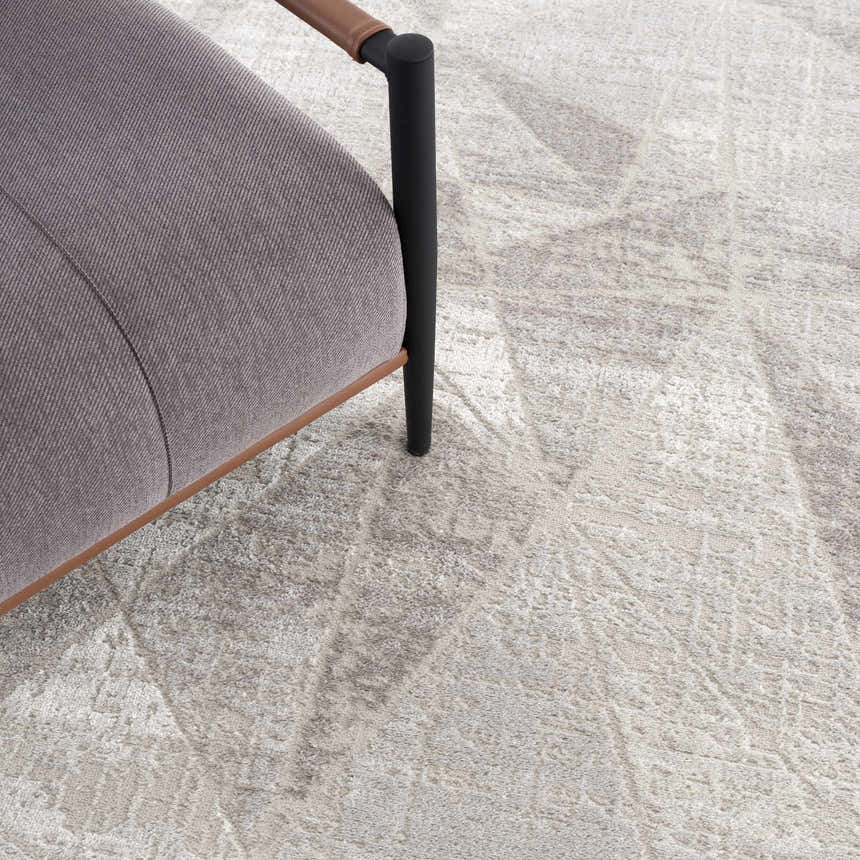 Close-up of gray Basia Area Rug with a subtle geometric pattern, styled with a modern gray chair. Styleshot