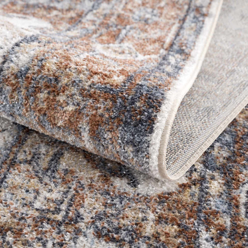 Close-up of the Rust Hera Washable Area Rug showing its rust, blue, and off-white vintage-style pattern and soft texture. Fold