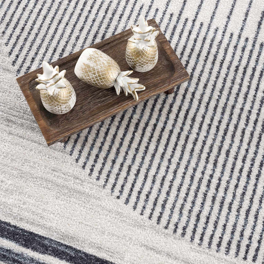 Close-up of the Thad Medium Gray Washable Area Rug with a geometric stripe pattern and decorative pineapples. Styleshot