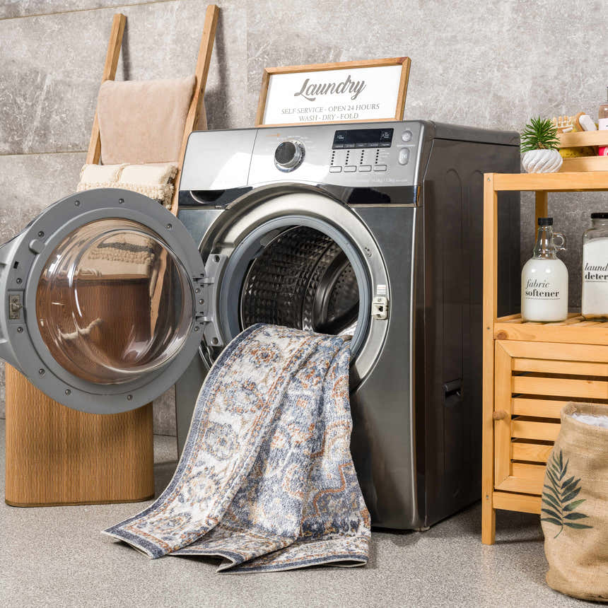 Laundry room scene with Aurum Blue & Beige Washable Area Rug partially inside a washing machine. Farmhouse style decor. Washing-Machine