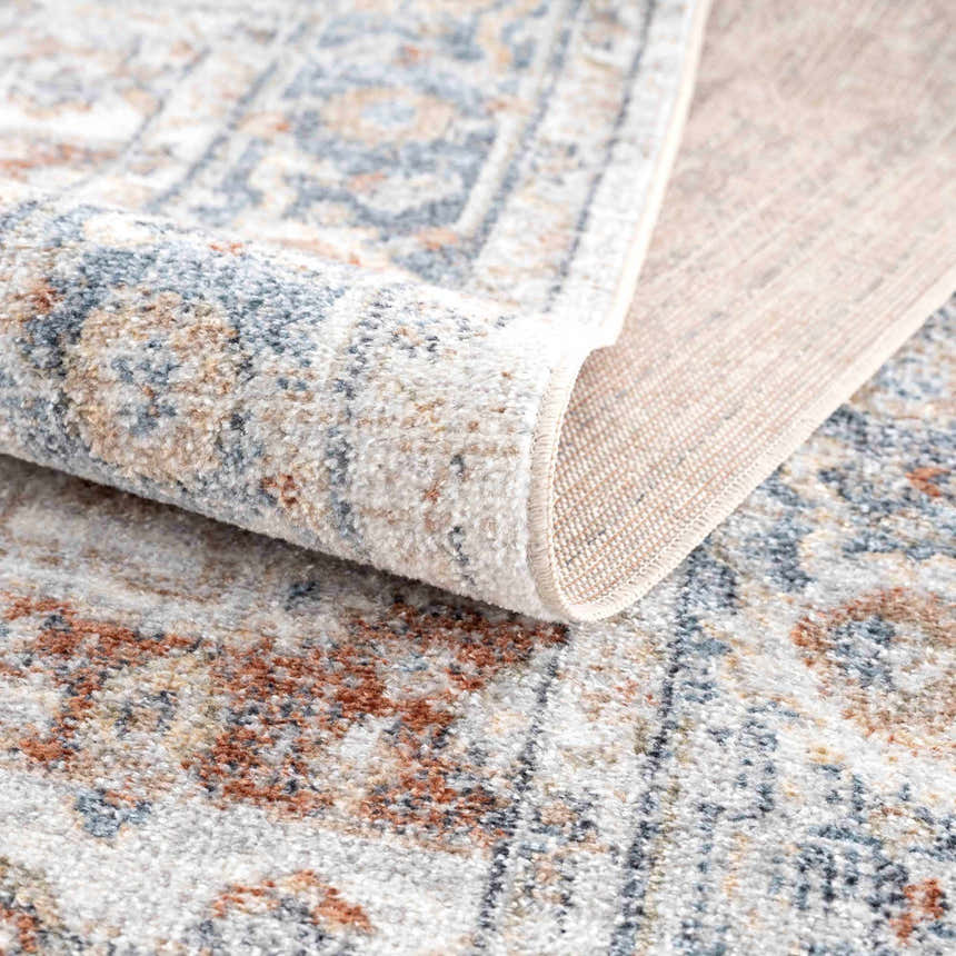 Close up of the Neta Red & Blue Washable Rug showing its flat pile, oriental pattern, and colors like driftwood and nutmeg. Fold