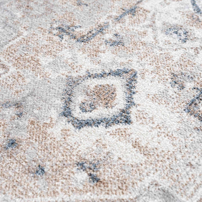Close-up of the Dobry Boutique Washable Rug. Features a blue, tan, and off-white traditional pattern and soft texture. Texture