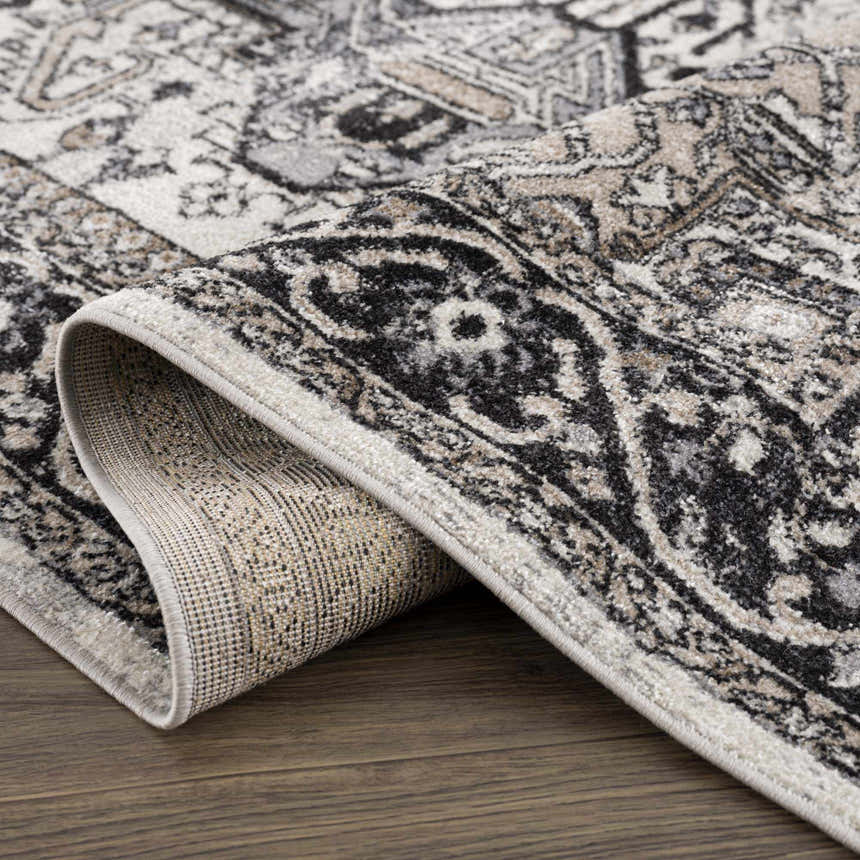 Close-up of the Cabacungan Washable Area Rug. Bohemian vintage design in black, gray, light beige, and taupe colors. Fold