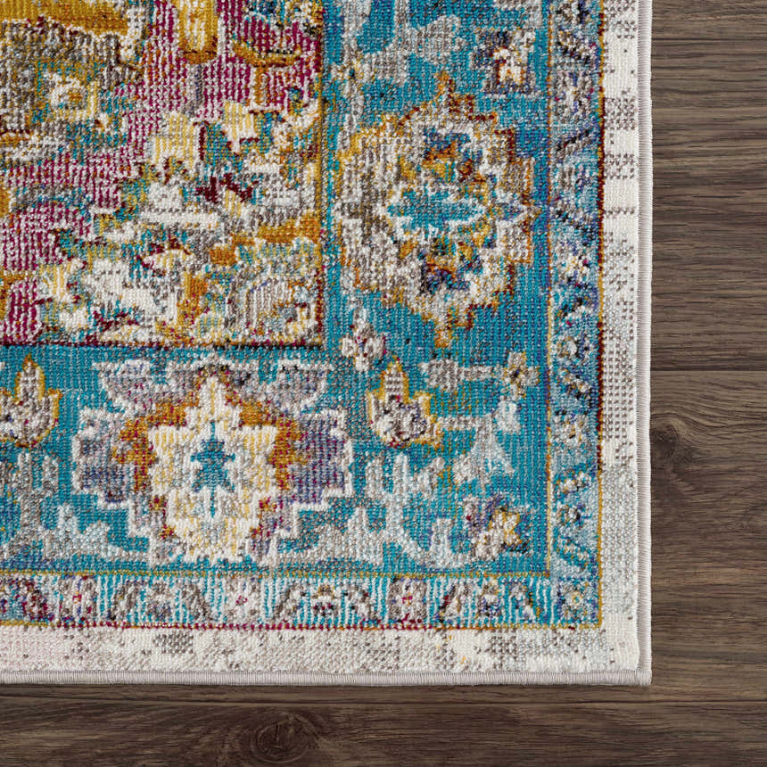 Close-up of the Mardin Colorful Area Rug showing its blue, pink, and mustard vintage-style pattern on a dark wood floor. Swatch