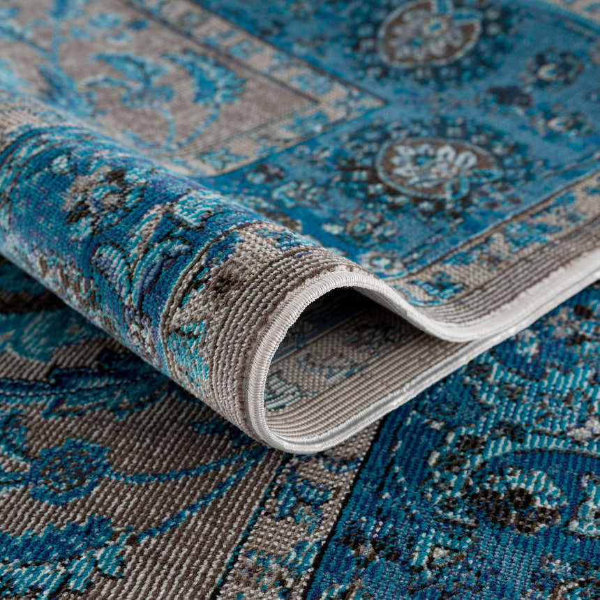 Close-up of the Mardina Turquoise Area Rug showing its beige and turquoise vintage-inspired pattern and machine-woven texture. Fold
